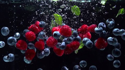 Raspberries, Blueberries and fresh mint leaves splashing into water on black background. Falling fresh fruits and berries in water. Organic berry, healthy food, diet 4K UHD video 3840X2160 slow motion