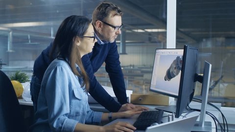 Female Industrial Technician and Male Chief Engineer Designing 3D Turbine/ Engine Model with Help of Cad Software. They Work on a Computer with Two Displays. Shot on RED EPIC-W 8K Helium Cinema Camera