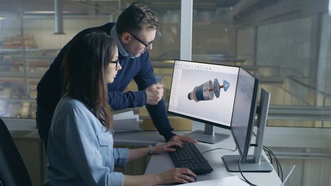 Female Industrial Engineer and Male Project Manager Work on 3D Turbine/ Engine Model in Her CAD Software. Inside of the Factory is Seen From the Office Window. Shot on RED EPIC-W 8K Helium  Camera.