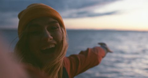 Happy Caucasian girl making selfie or a video call on a large lake, smiling and laughing into camera. Smartphone camera POV. 4K UHD