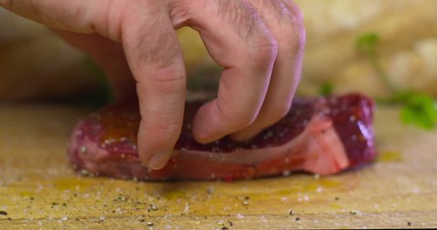 Man flips over seasoned and oiled raw beef fillet steak on wooden chopping board. Slow Motion