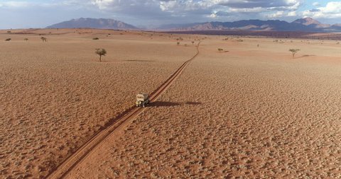Aerial view of a safari vehicle driving through the vast plains of the NamibRand Nature Reserve, Namibia