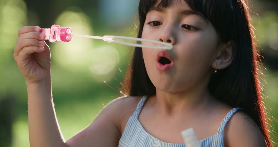 close-up of Happy little Asian girl blowing soap bubbles in spring Park. Slow motion