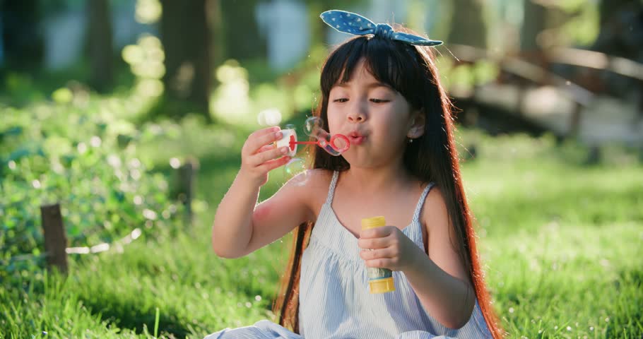 close-up of Happy little Asian girl blowing soap bubbles in spring Park. Slow motion