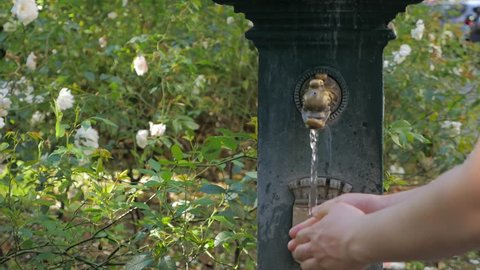 Man drinking water and washing hands from ancient oriental tap in the Milan, Italy. Hands under a stream of cool fresh water, outdoors in the summertime. Washing hands in natural green outdoor area.