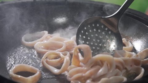 Rings of calamari are frying in the boiling oil on the open fire, grilling squid, seafood meal, asian cuisine, cooking outside
