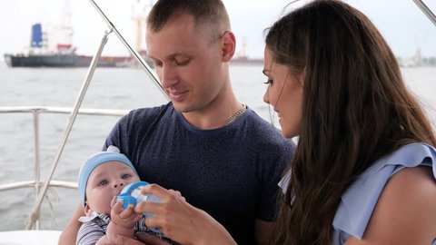 child eating his first fruits in hands daddy, family with baby on vacation, parents and children on sea, happy couple in yacht, mom, dad and son outdoors, healthy eating child's