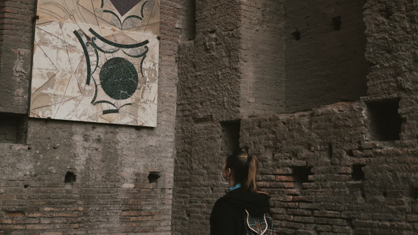 Young beautiful tourist is in Palatine Hill in Rome, Italy, considering an antique aesthetic wall-painting of ancient.