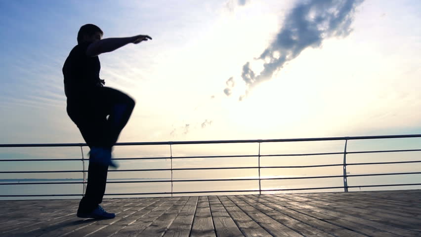 Handsome sportsman jumping and kicking on the wood pier in slow motion