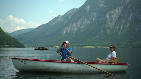4k travel video, active senior couple sitting in rowboat on austrian mountain lake enjoying landscape and taking pictures
