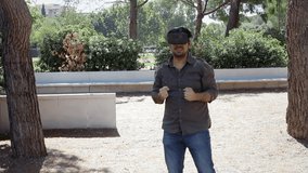 A man in a park, with a virtual reality headset, fighting while playing a video game. Handheld shot. Simple coloring.
