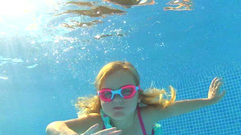 Underwater view young girl wearing goggles waving at camera. Vídeo Stock
