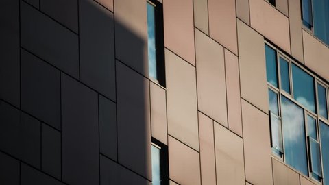 Time lapse of shadows falling on to the facade of a modern building. Clouds reflect of the windows. 