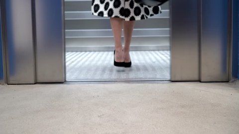 Woman in a skirt get out of an elevator. Close-up of legs