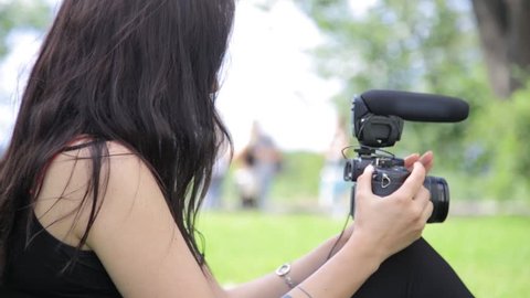 Young mixed race female indie film maker shooting in a green natural setting with grass on background. DSLR camera with microphone.