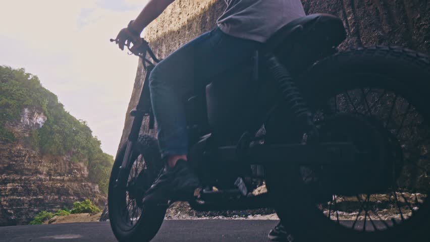 Motorcyclist driving his motorbike Between two rocks on the ocean beach