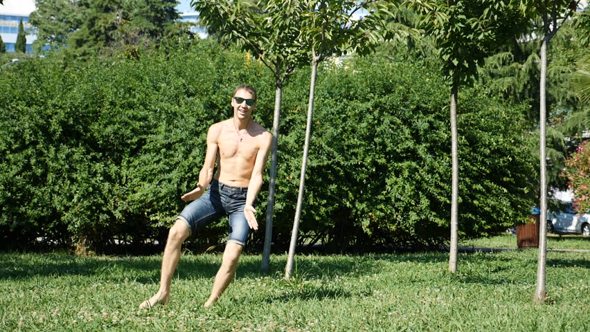 A young happy guy with a bare torso dancing modern ballet and wacking in a summer park. slow-mo
