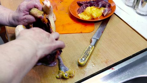 A woman is carving a bird on a cutting wooden board at home in the kitchen. She gets inedible guts. Edible viscera are located in an orange plate