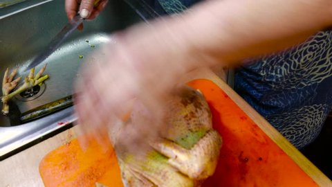 Chef at home kitchen cuts bird's ass on the orange cutting board nearly the tap