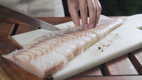 Chef is slicing raw codfish on the board before roasting it, cooking outdoors, fish grill and barbecue
