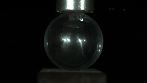 Glass Sphere Smashed Under Pressure Slo-Mo - A shiny glass sphere shatters apart in slow motion as it is smashed between a wooden block and a metal rod Stockvideo