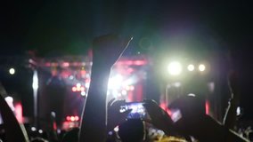 audience at concert or party shoot video by means mobile telephone, people on concert shoot foto using android, slow motion, lit scene night rock festival, many lights on stage