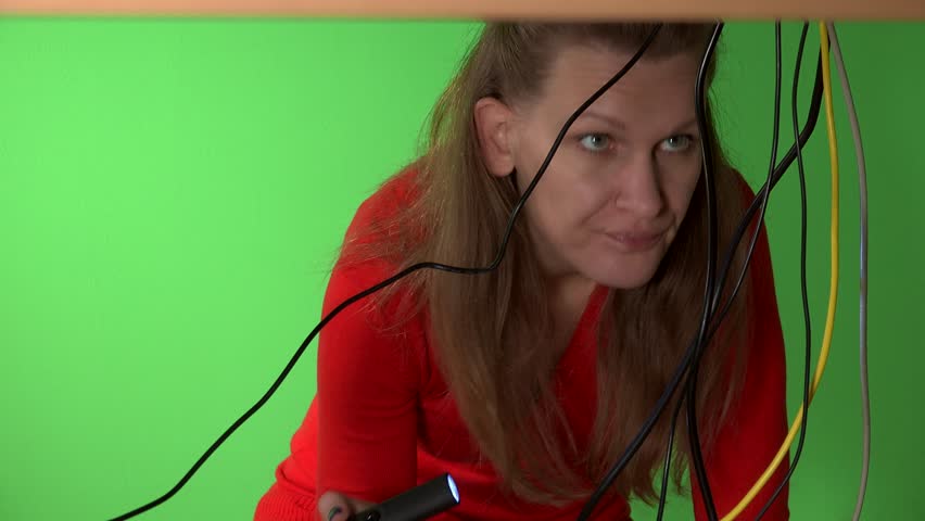 Business woman trying to repair computer with flash light under table. Green wall background. Static closeup shot. 4K UHD