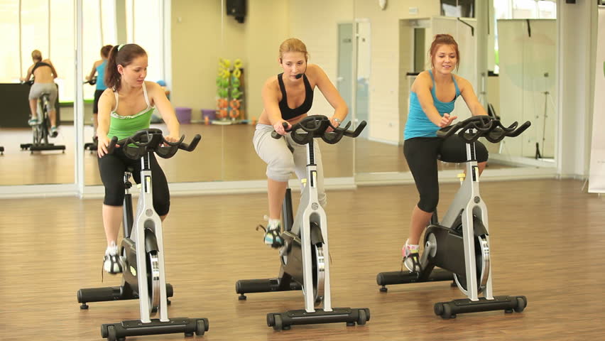 Group of slim girls training on cycles with instructor