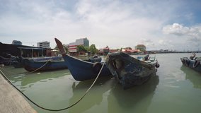 Row of old. wooden fishing boats. tied to a wooden pier in Penang Malaysia. under a partly cloudy sky. UltraHD 4k video