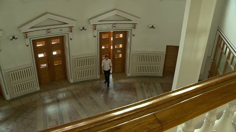 A view from above through the railing of the balcony, a young man enters the inside of a large old building