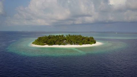 The camera is approaching round tropical island resort hotel with white sand palm trees and turquoise Indian ocean on Maldives, drone footage aerial view from above in 4k