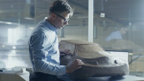 Senior Automotive Designer with Rake Sculpts Futuristic Electric Car Model from Plasticine Clay. He Works in a Special Studio Located In a Large Car Factory.Shot on RED EPIC-W 8K Helium Cinema Camera.