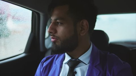 Young muslim businessman riding in the car on passenger's seat. Rain outside the car. Passenger in taxi