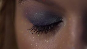 A female eye with blue make-up and glitter is blinking.