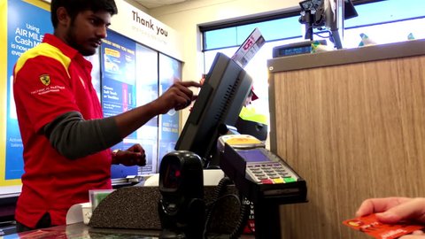 Coquitlam, BC, Canada - July 13, 2017 : Woman buying lottery ticket and tapping credit card at check out counter inside Shell gas station convenient store with 4k resolution