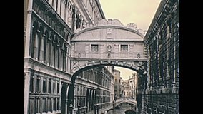 Historical archive footage of Venice narrow canals and its small historic bridges through the alleys of the town. Detail of romantic Ponte dei Sospiri arcade bridge.