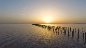 Abandoned destroyed wooden pier on lake at sunset, aerial video  / Water surface in golden glow of sunset, aerial video