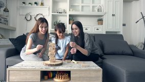 Young girl playing game with mother and asian nanny in living room. Beautiful white child playing block with her mother and pretty young asian nanny at home in the afternoon.