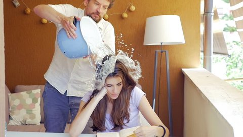 Man making joke to girlfriend splashing bucket of cold water on head slow motion