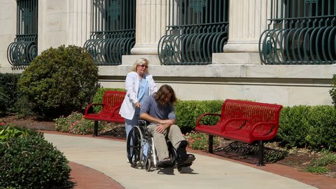 Nurse pushes a depressed mental patient in a wheelchair along the sidewalk outside a state facility for the mentally insane.
