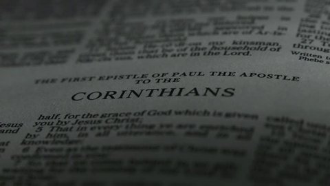The Bible-  A slow, shallow depth of field, candle lit pan across a page of the Bible that  reveals the heading for the book of 1st Corinthians.