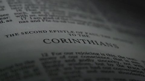 The Bible-  A slow, shallow depth of field, candle lit pan across a page of the Bible that  reveals the heading for the book of 2nd Corinthians.