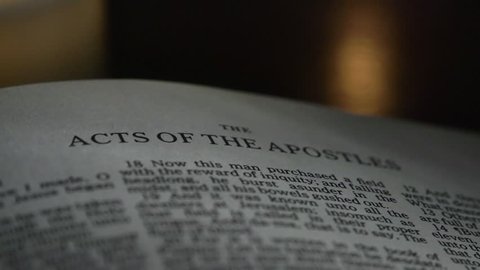 The Bible-  A slow, shallow depth of field, candle lit pan across a page of the Bible that  reveals the heading for the book of Acts.