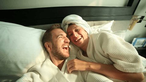 Young couple taking selfie in hotel bed
Young funny couple on a comfortable bed in an hotel room taking a selfie in the morning. They both wearing a bathrobe and the woman a towel on her hair.