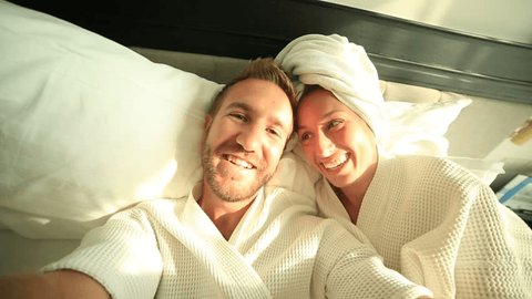 Young couple taking selfie in hotel bed
Young funny couple on a comfortable bed in an hotel room taking a selfie in the morning. They both wearing a bathrobe and the woman a towel on her hair.