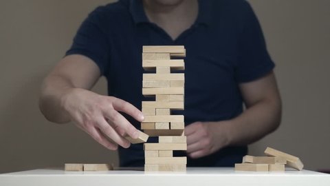 Timelapse loop of assembilng and disassembling Jenga Tower. IT man is playing Jenga game and disassembling the tower. Taking bricks out one by one and putting them back together. Perfect Skills.