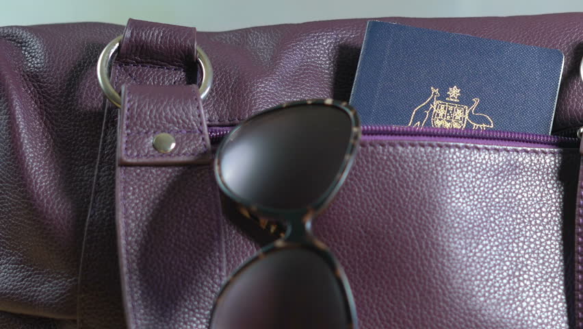 Travel concept with woman taking passport out of carry bag with sunglasses, with light flare, closeup.