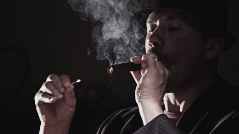 A Man Smokes a Cigar. Takes a big drag and puffs smoke.