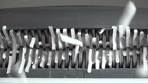 Cut paper strips tumble from paper shredder blades, fall onto camera lens. 4K UHD 3840x2160
