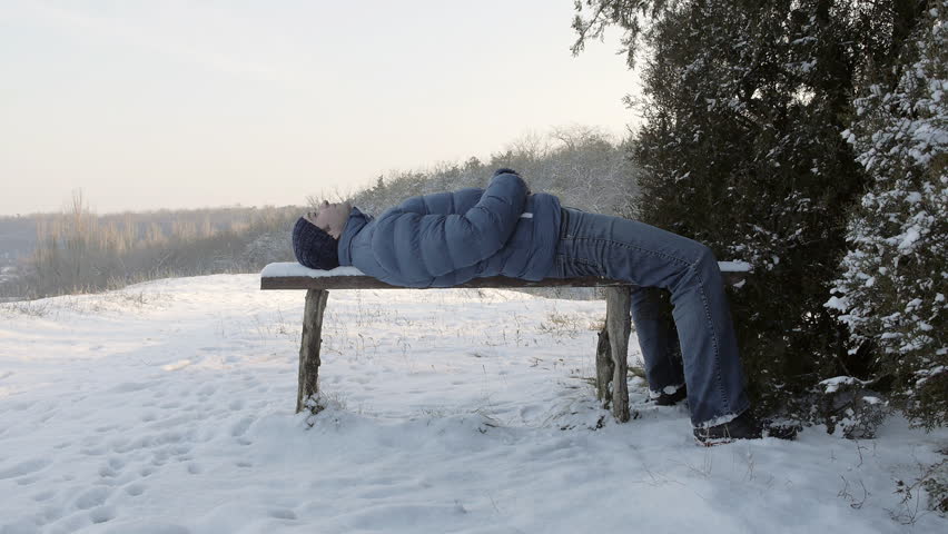 A man, lying on a snow-covered bench and enjoying the beautiful winter landscape